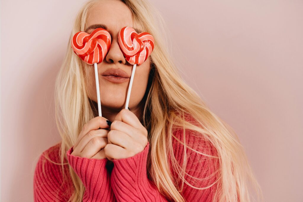Woman covering her eyes with heart shaped lollipops